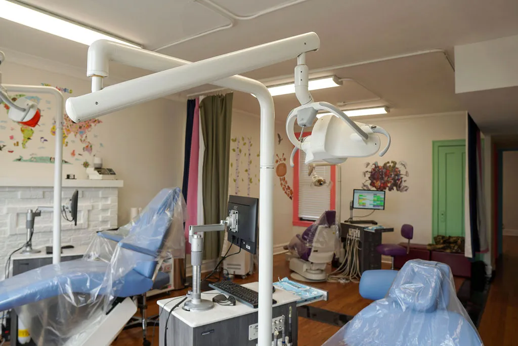 A wide view of a professional dental surgery room with blue patient chairs, overhead medical lighting, and clinical equipment.