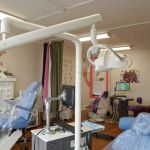 A wide view of a professional dental surgery room with blue patient chairs, overhead medical lighting, and clinical equipment.