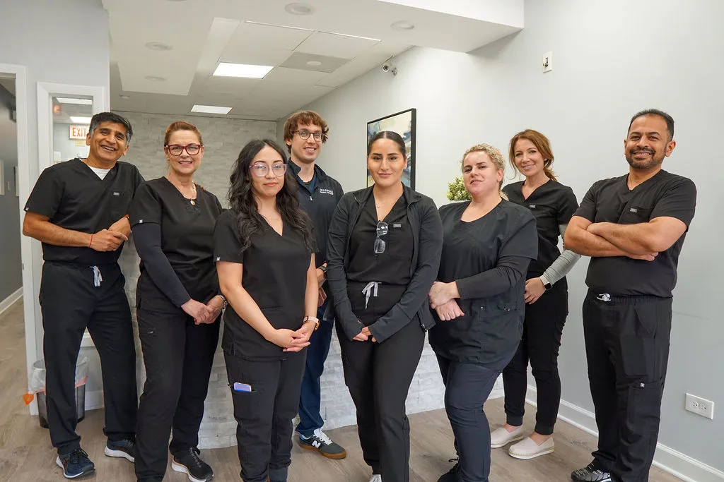 A professional team of seven dental staff members wearing matching black scrubs, standing together in a hallway and smiling.