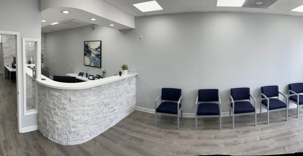 A clean, white curved reception desk in a dental office with a row of blue chairs for waiting patients in the background.