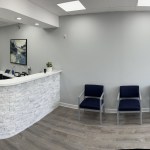 A clean, white curved reception desk in a dental office with a row of blue chairs for waiting patients in the background.