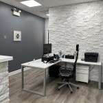 A modern dental consultation room featuring a white desk with a computer monitor and a textured white accent wall.